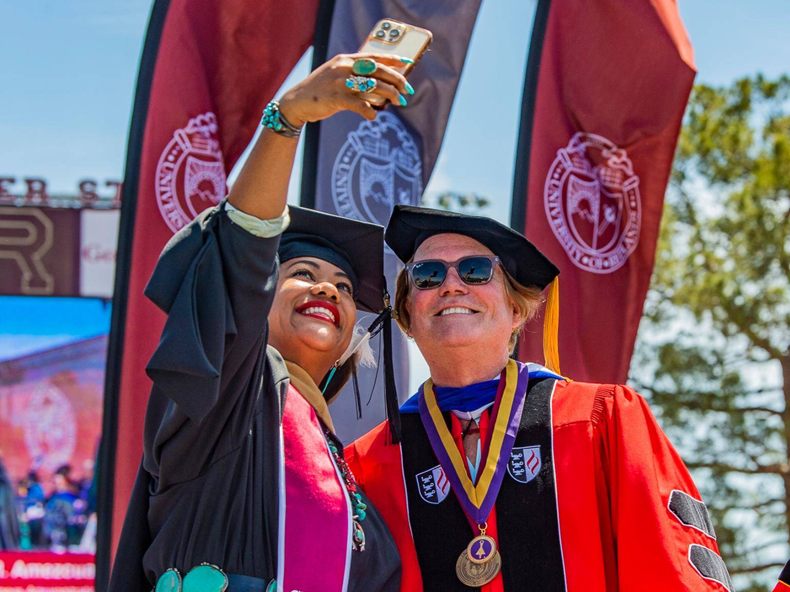 a woman taking a selfie with a man in graduation gown