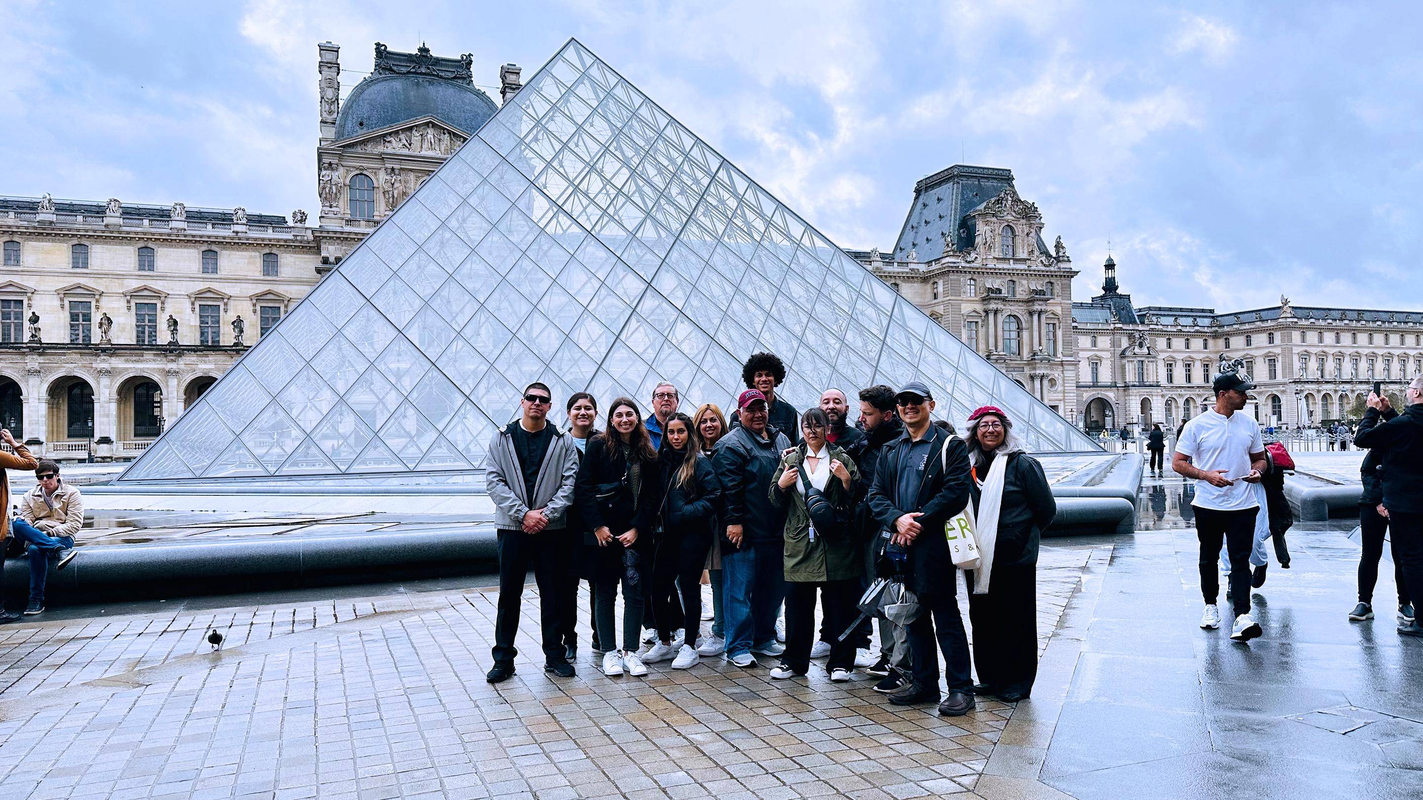 a group of people posing for a photo in front of a glass pyramid