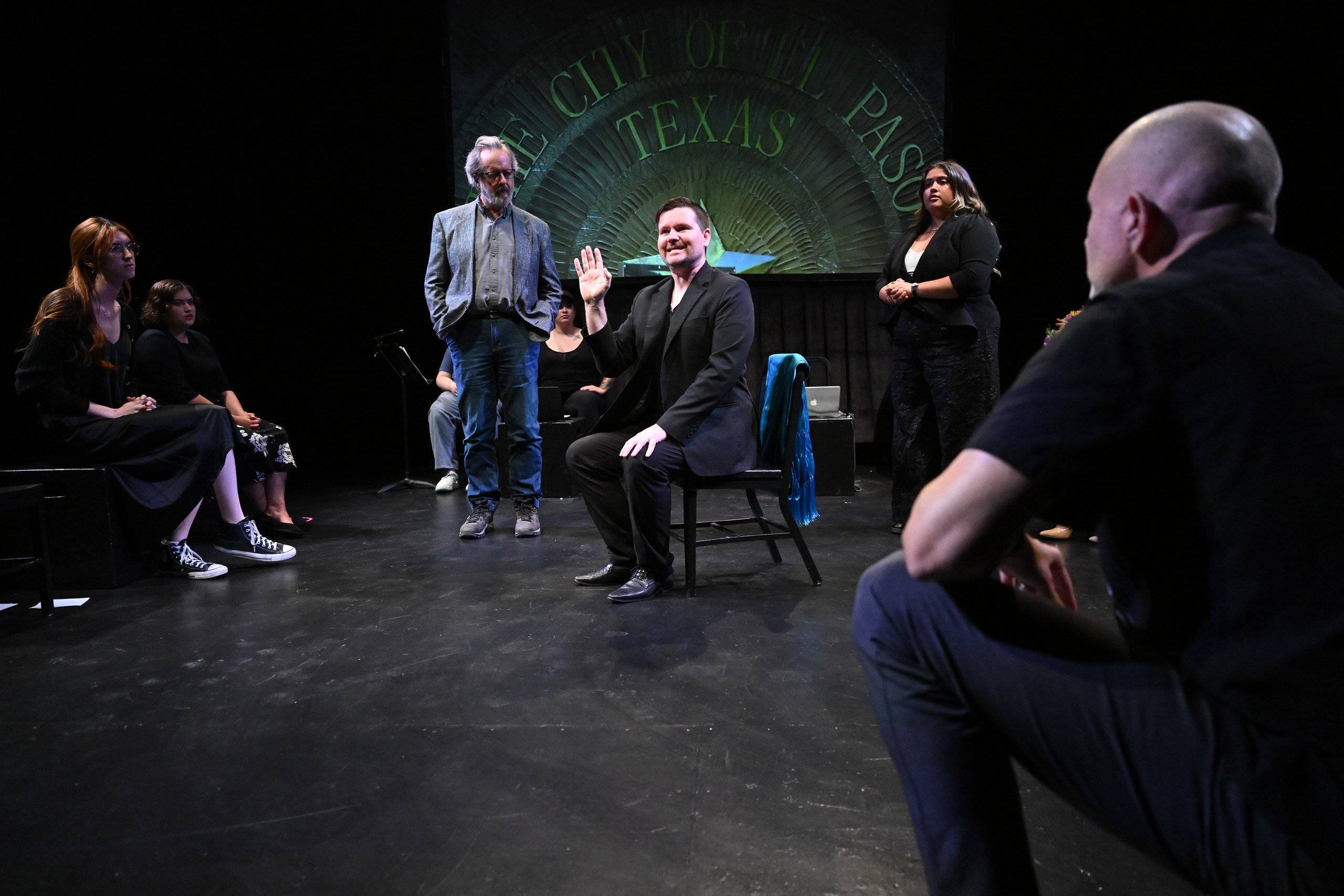 a man sitting in a chair on a stage with people watching