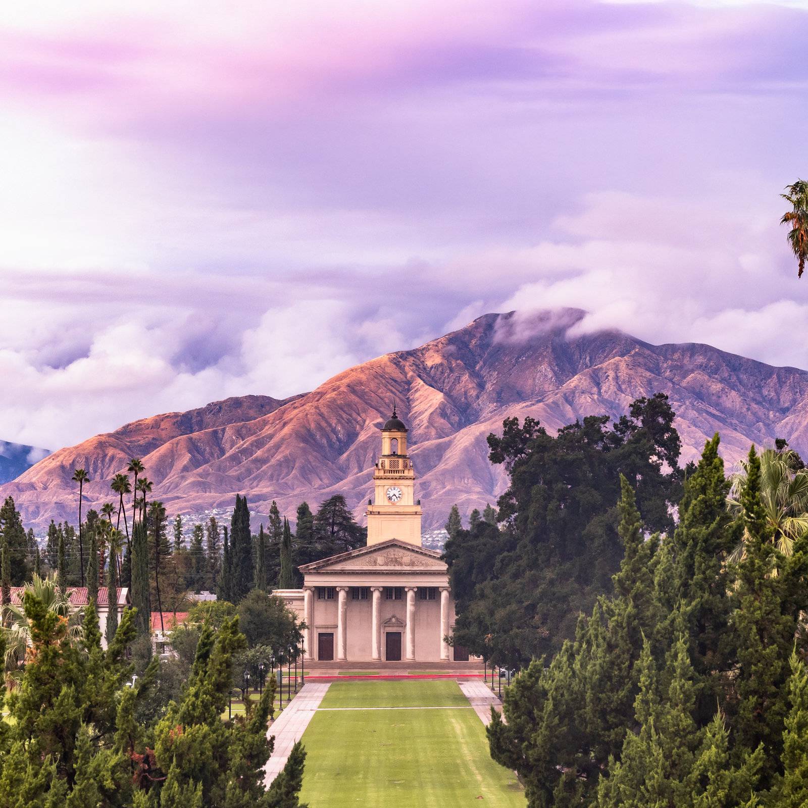 a building with a clock tower and trees and mountains in the background