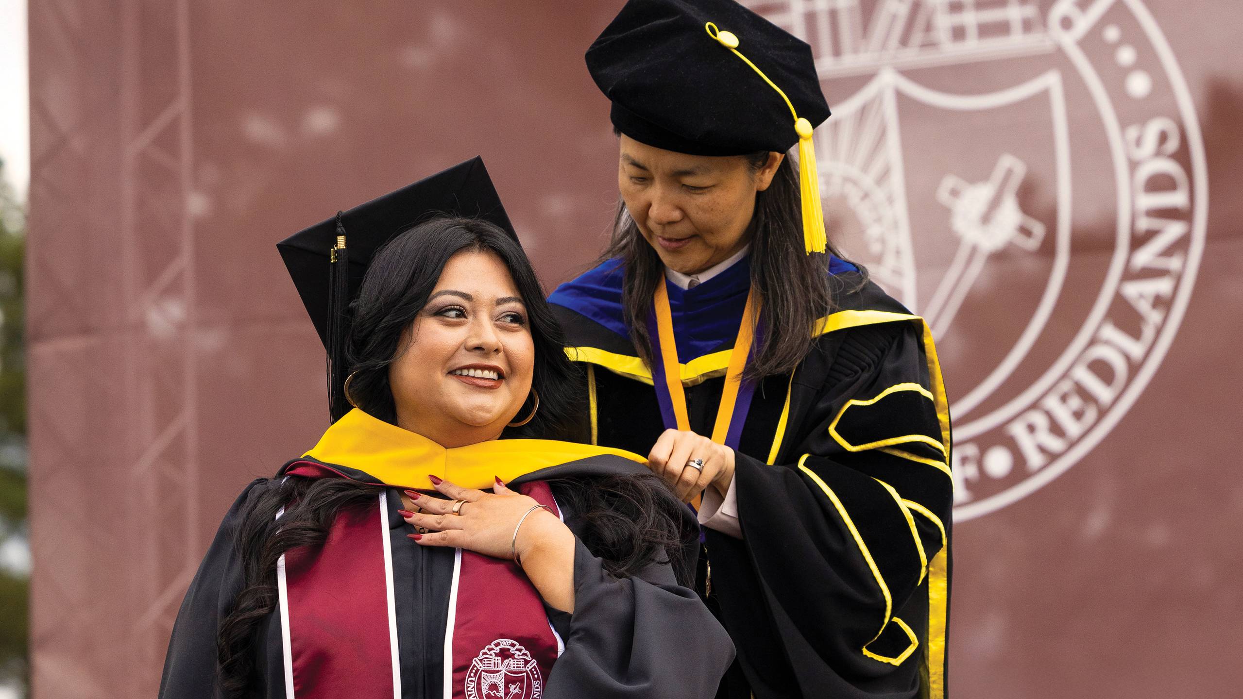 A professor putting on a yellow scarf for a graduate student.