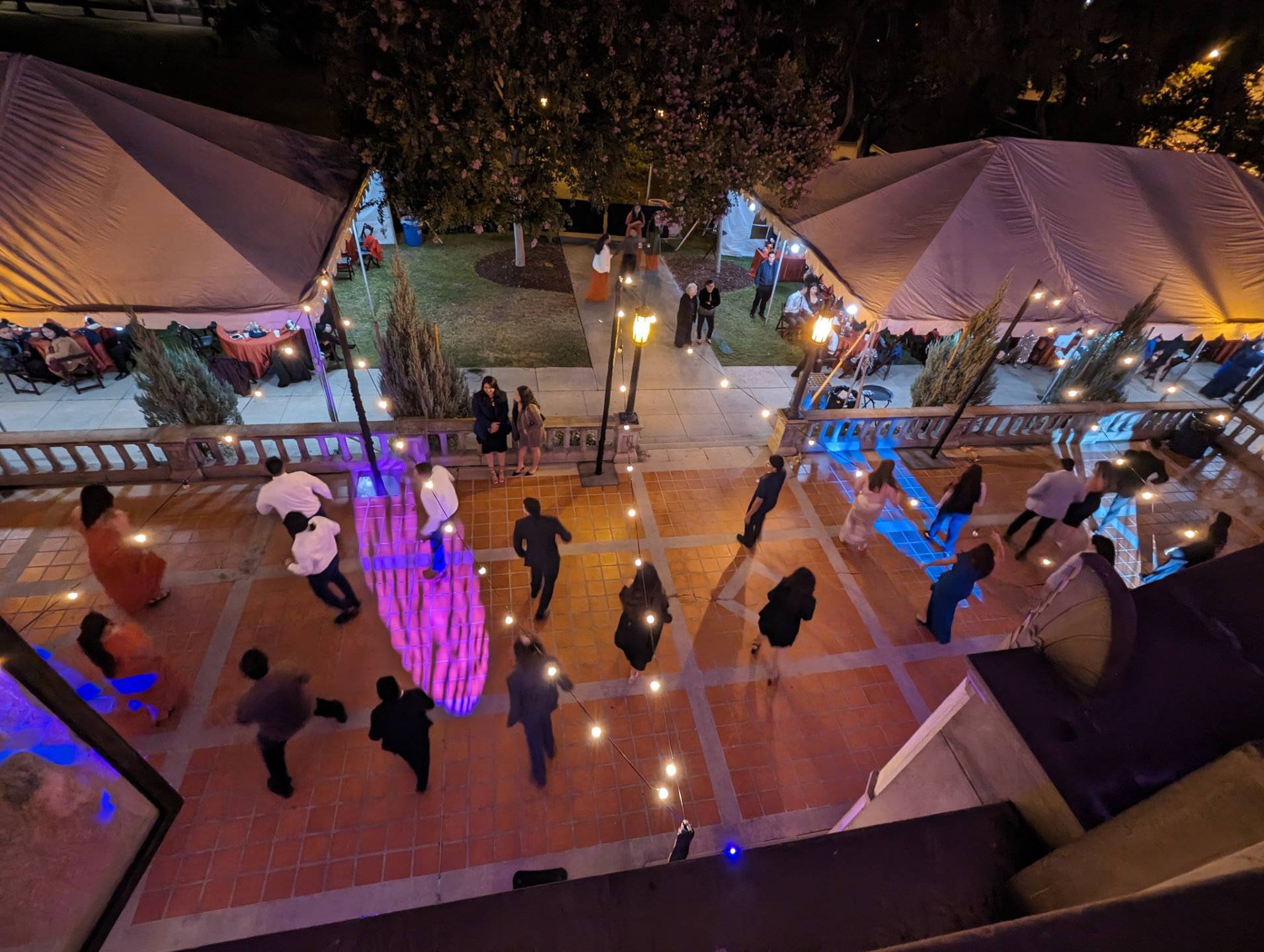 a group of people walking around a courtyard with tents and trees