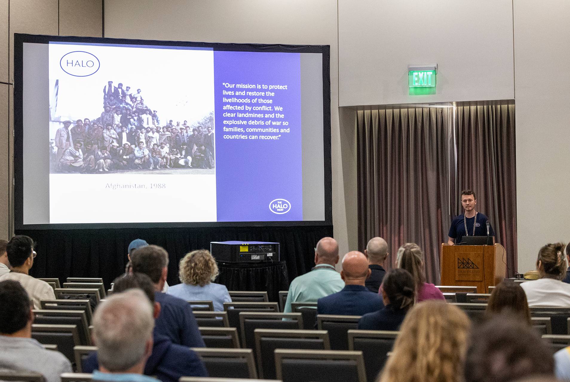 a man standing at a podium in front of a large screen