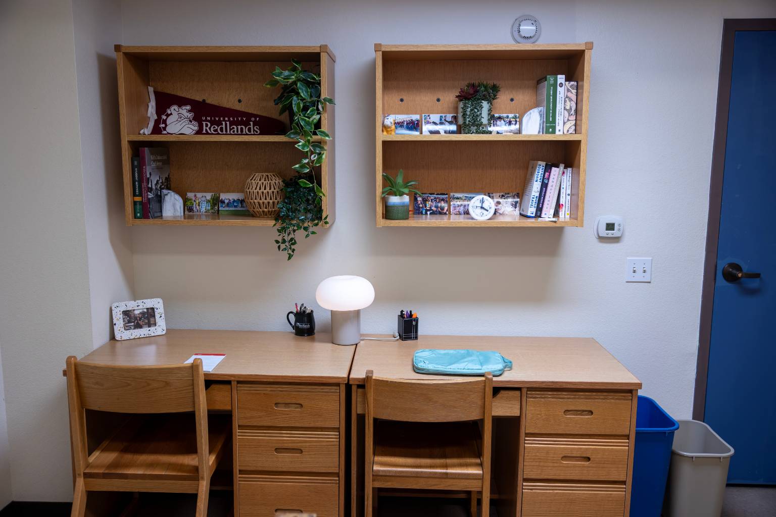 a desk and chairs with a lamp and books on the wall