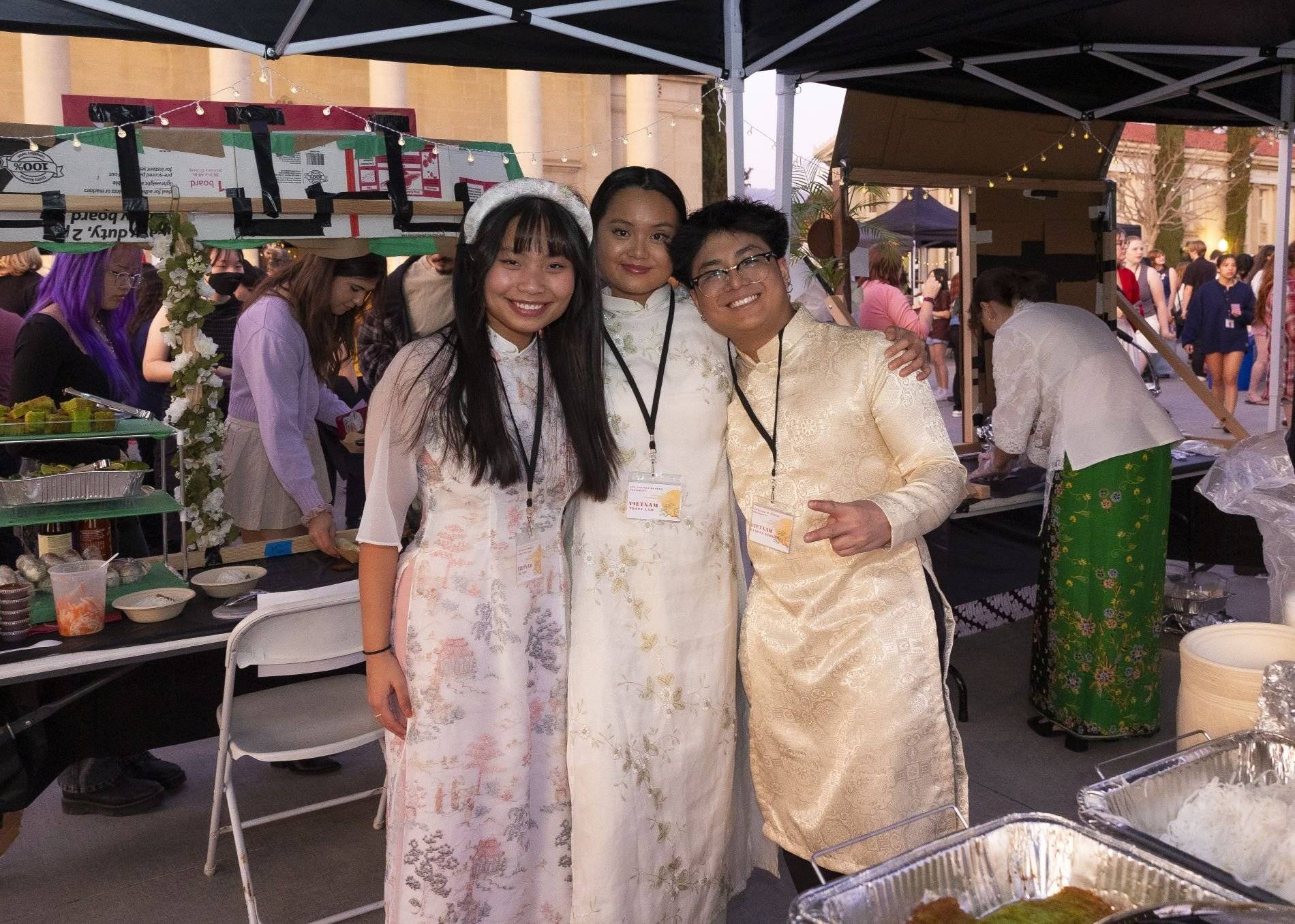 Three students stand together in traditional attire at a booth during the Asian Student Association Night Market.