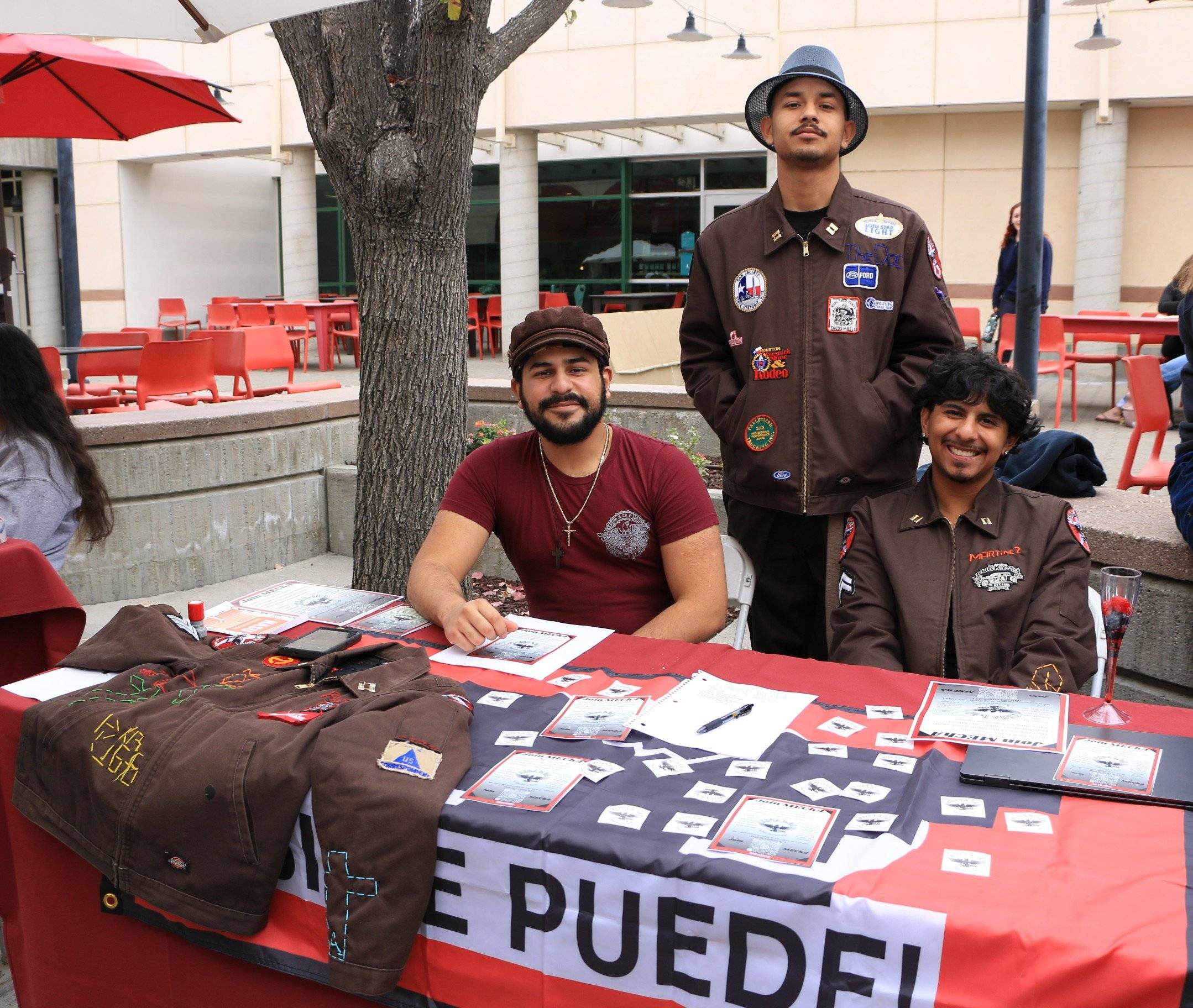 Three students pose behind a table displaying decorated jackets and printed materials at the Involvement Fair.