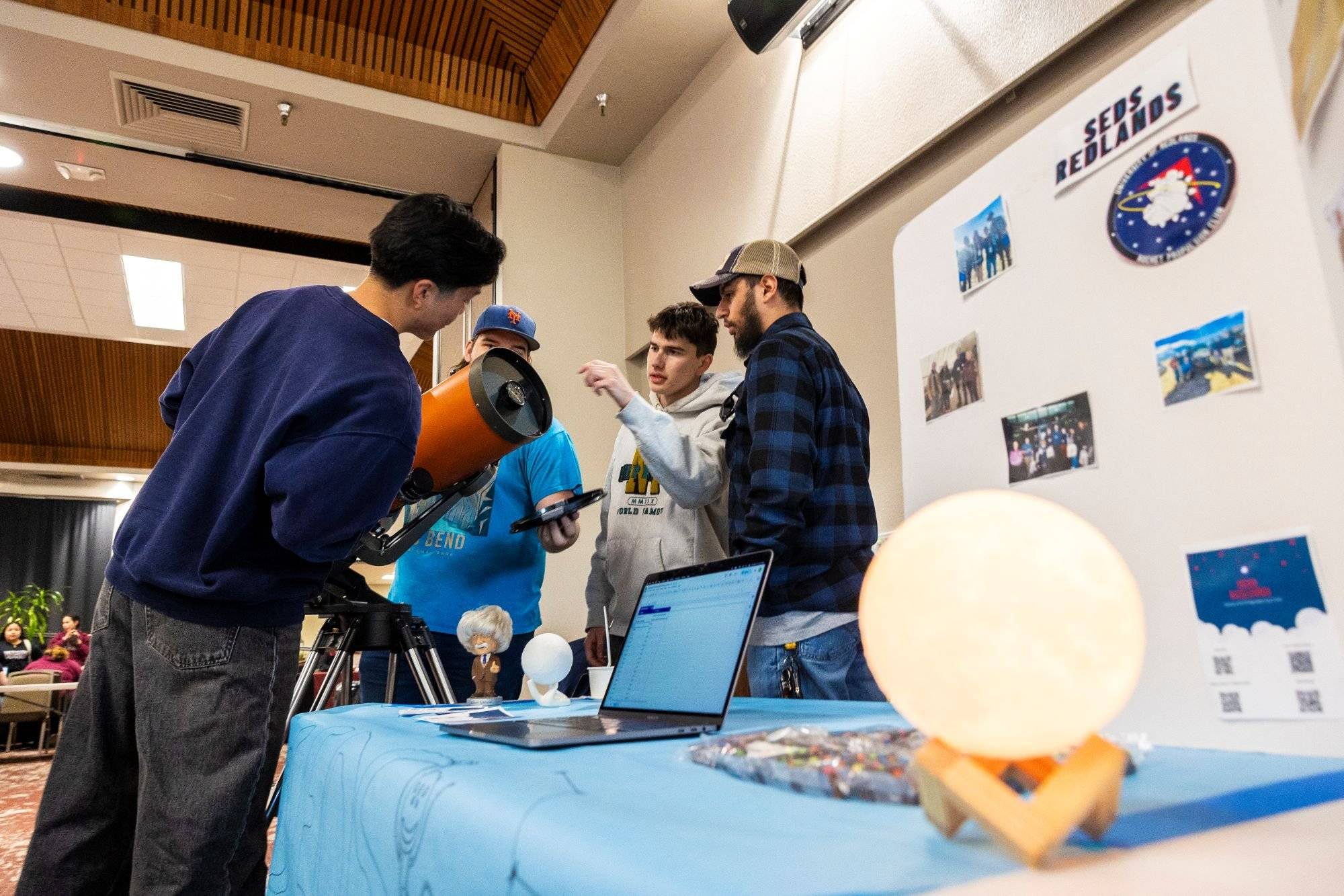 A group of students examine an orange telescope at an Involvement Fair club booth.