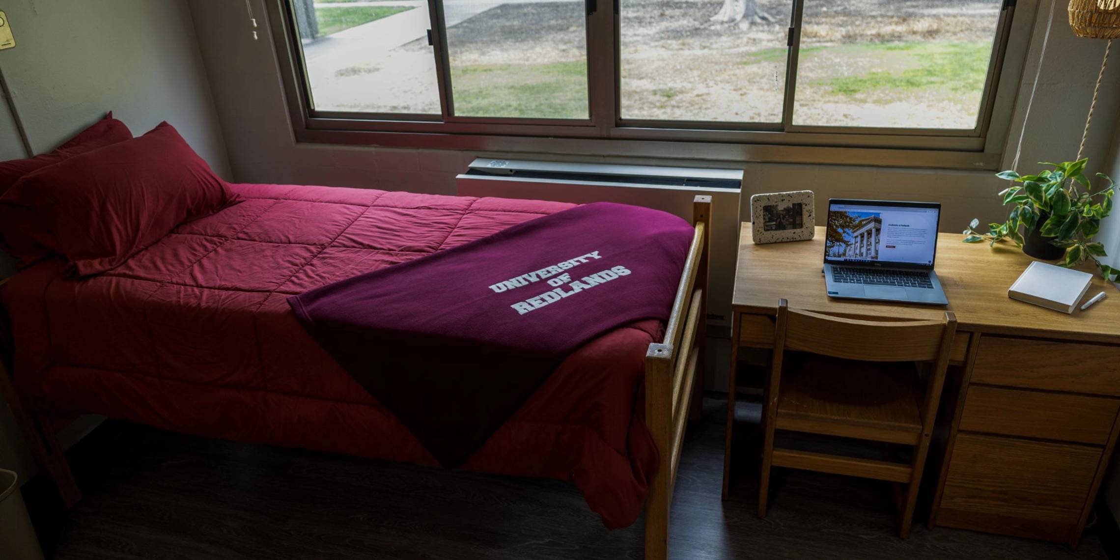 a bed with a red blanket and a desk next to a window