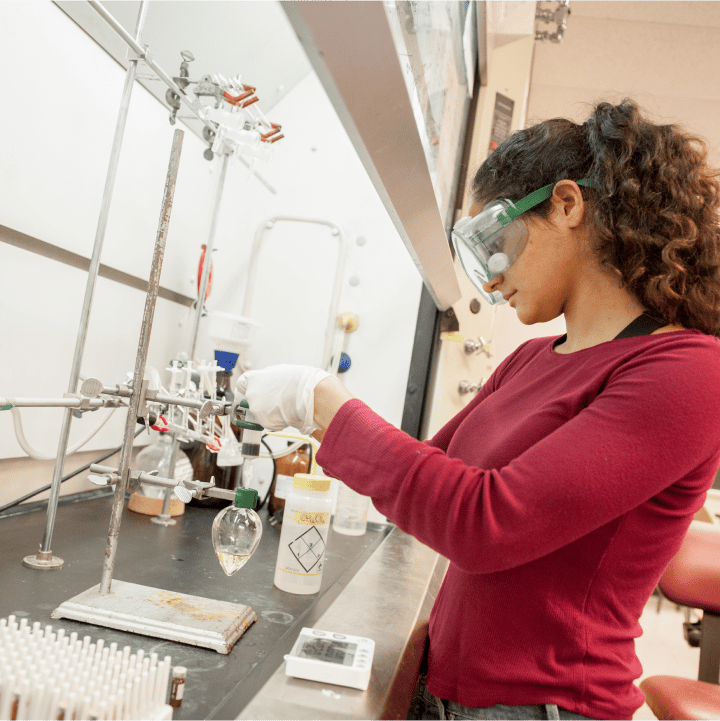 a woman wearing safety goggles and gloves working in a lab