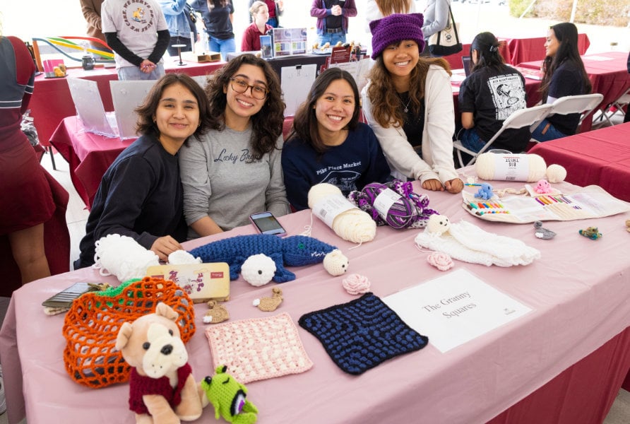 a group of women sitting at a table with crochet crafts