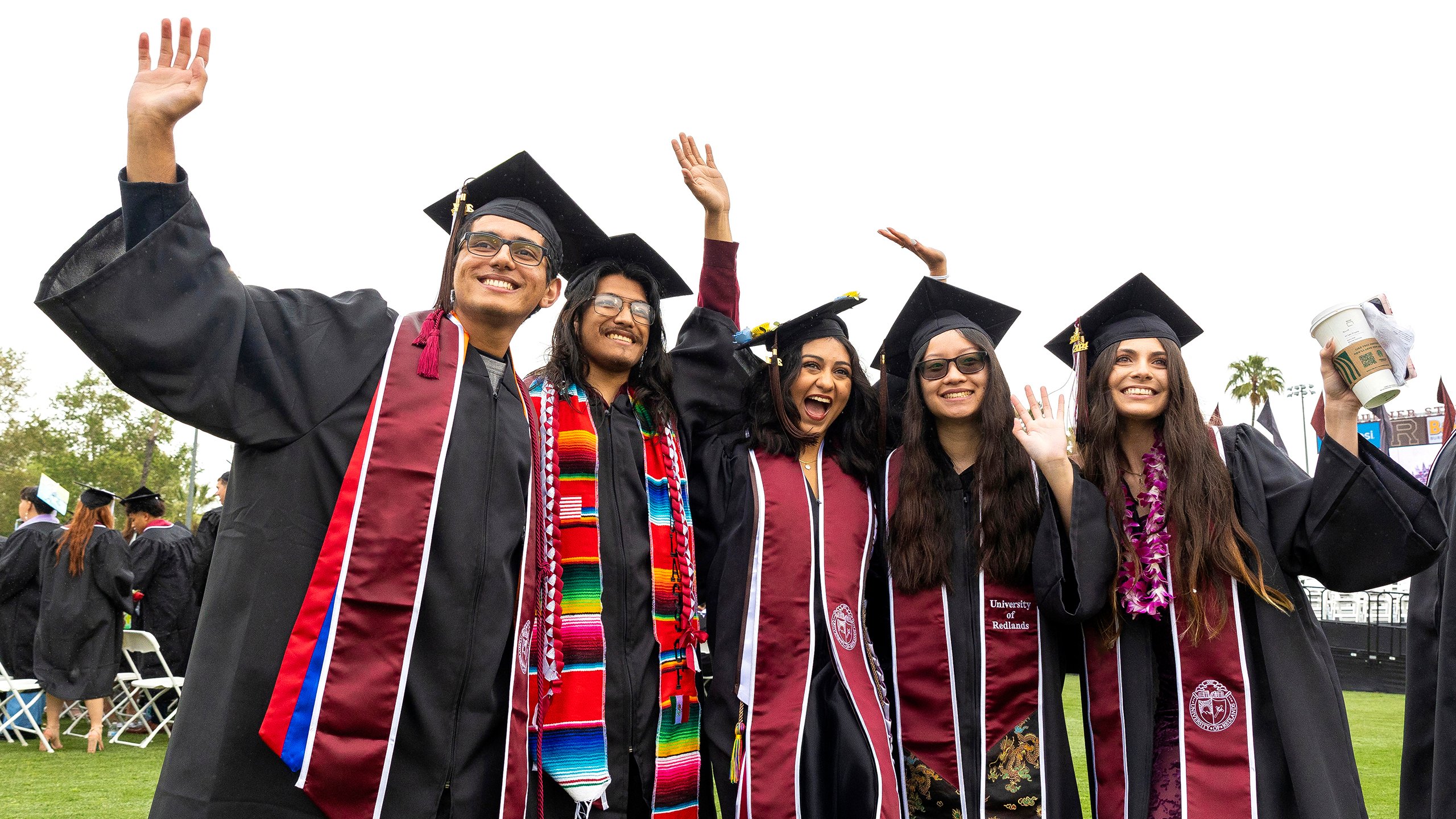 Graduate students smiling and waving in their caps and gowns.