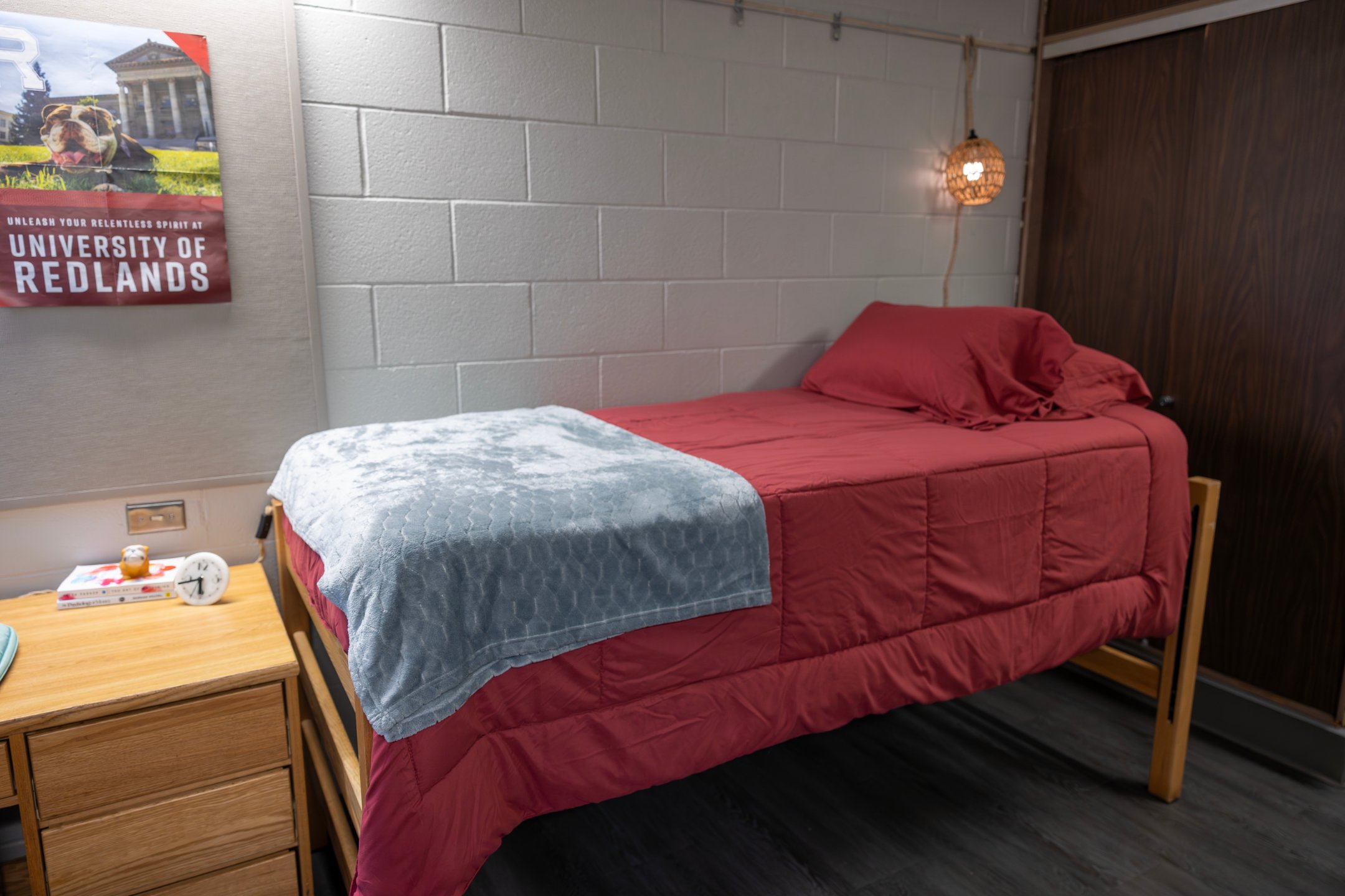 a bed with a red blanket and a lamp on the wall