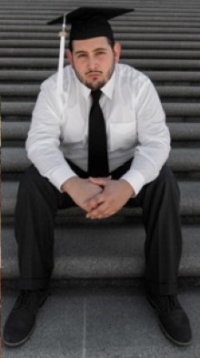 Javier Garcia III seated on outdoor steps wearing formal attire and a graduation cap.