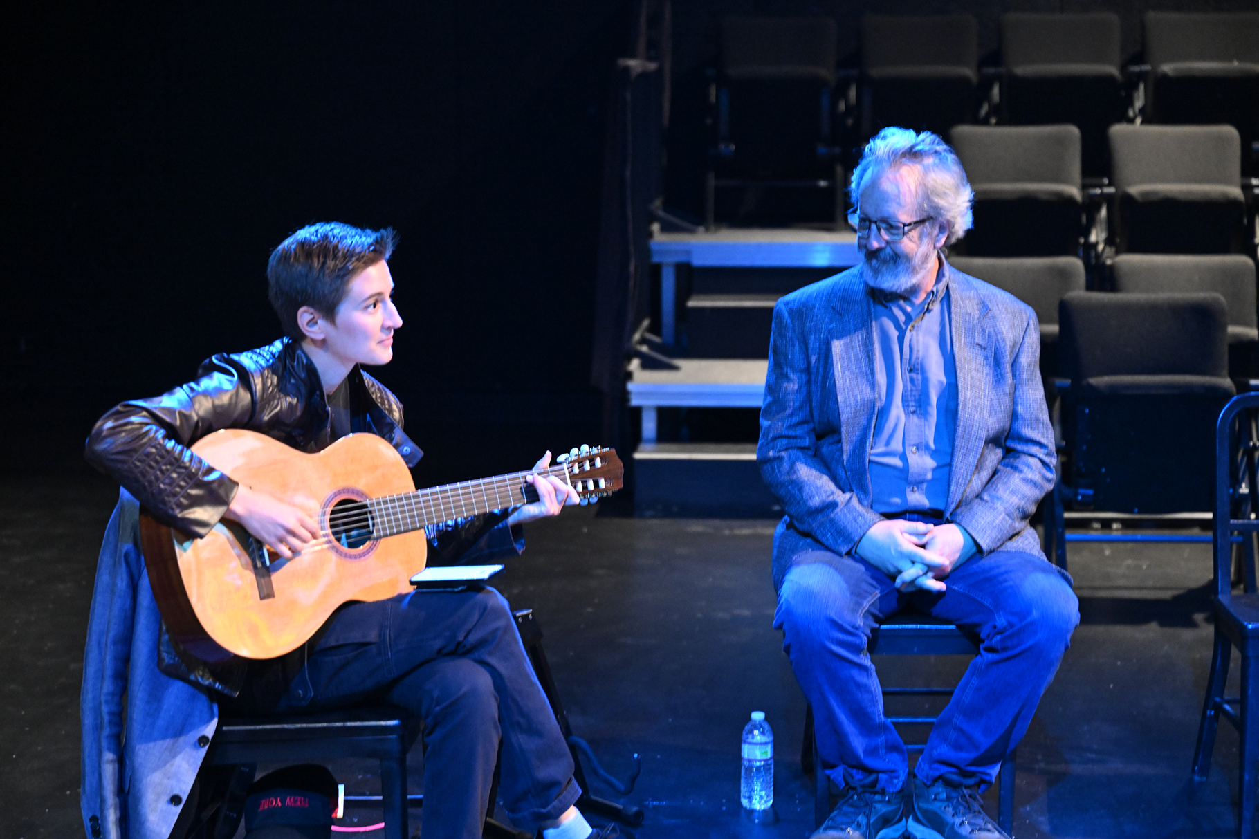 a man playing guitar next to a man sitting on a stage