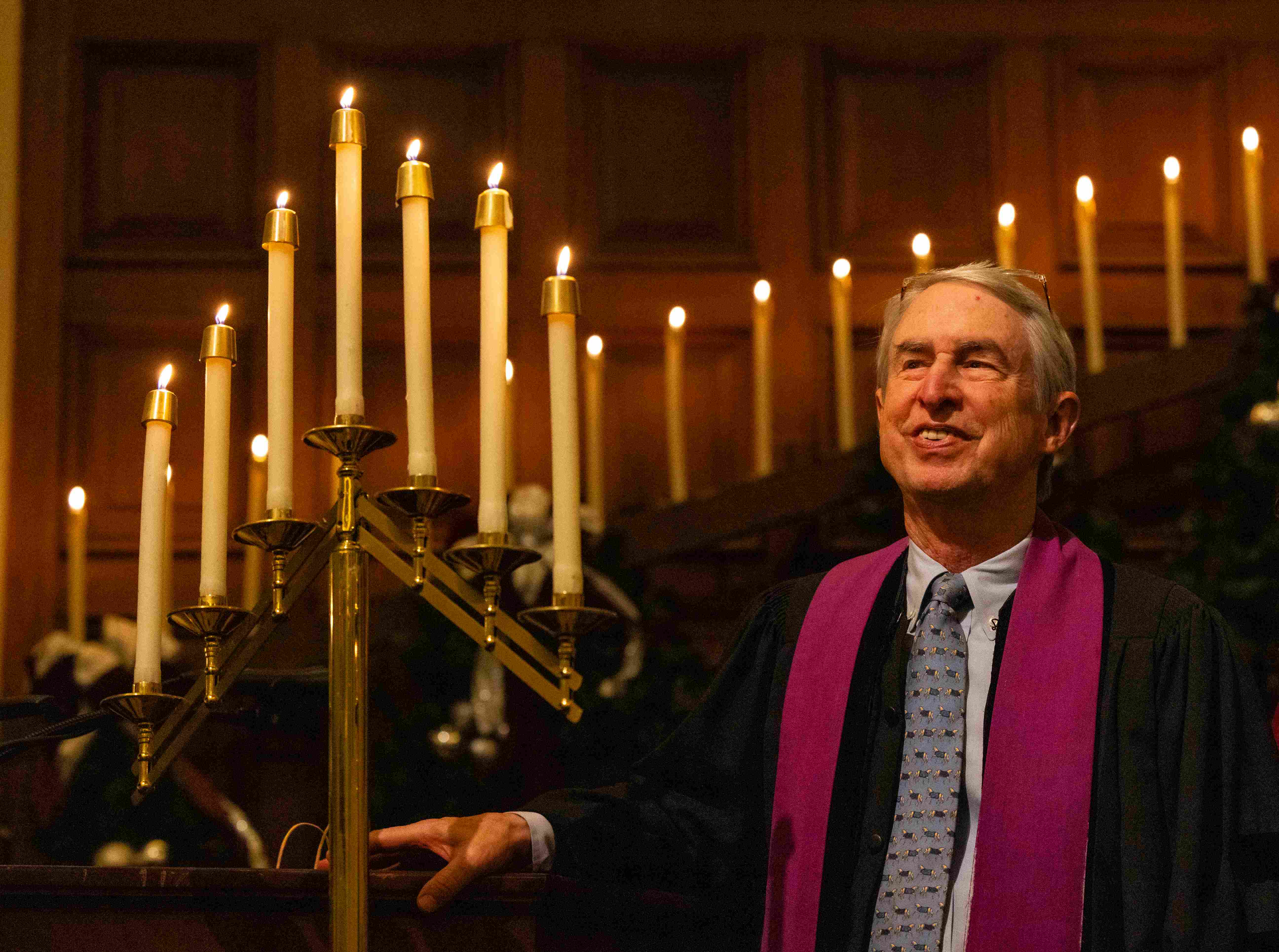 a man in a robe and tie standing next to a lit candle